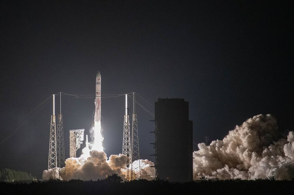 A rocket with side-mounted boosters lifts off from its pad at night amid a billowing cloud of exhaust.