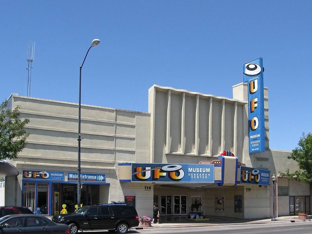 A downtown Roswell storefront museum with a tall UFO sign under a blue sky.